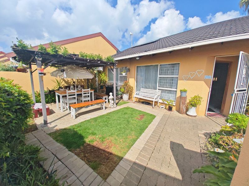 A private rear courtyard featuring a paved patio area, a timber pergola, and a small central lawn section.