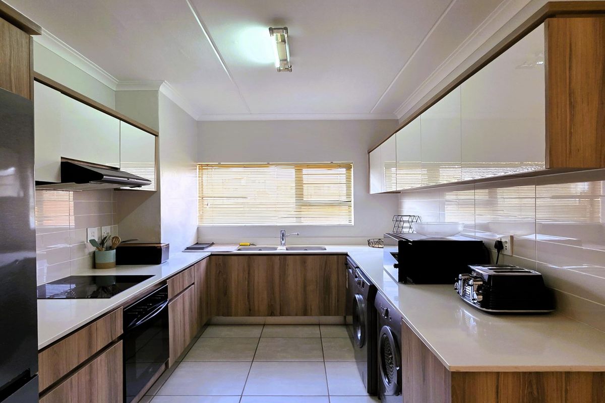 Modern galley-style kitchen featuring wood-grain cabinetry, quartz countertops, integrated appliances, and a tiled backsplash with ample storage and laundry utility space.