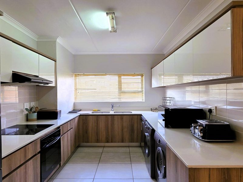 Modern galley-style kitchen featuring wood-grain cabinetry, quartz countertops, integrated appliances, and a tiled backsplash with ample storage and laundry utility space.