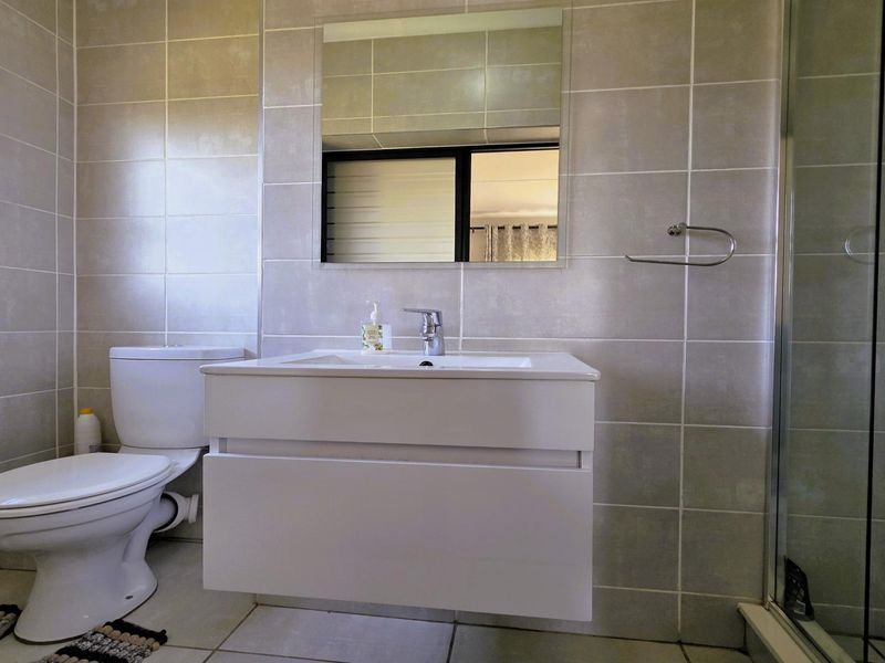 Modern bathroom featuring a wall-mounted vanity, ceramic basin, chrome mixer tap, toilet, and a glass-enclosed shower with neutral wall and floor tiling.