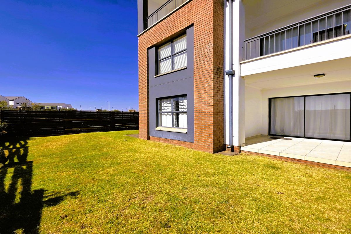 Rear view of the apartment building featuring a brick facade, a covered tiled patio with sliding glass doors, and a private lawn area.