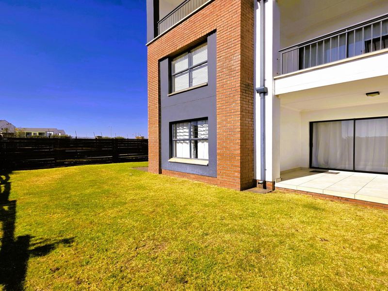 Rear view of the apartment building featuring a brick facade, a covered tiled patio with sliding glass doors, and a private lawn area.