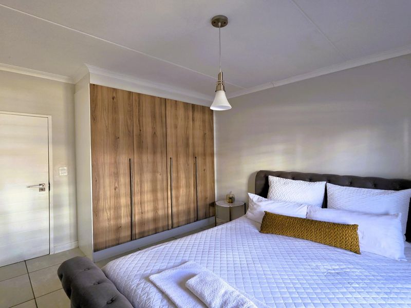 A well-maintained bedroom featuring modern wood-finish built-in wardrobes, neutral tiled flooring, and a contemporary pendant light fixture.