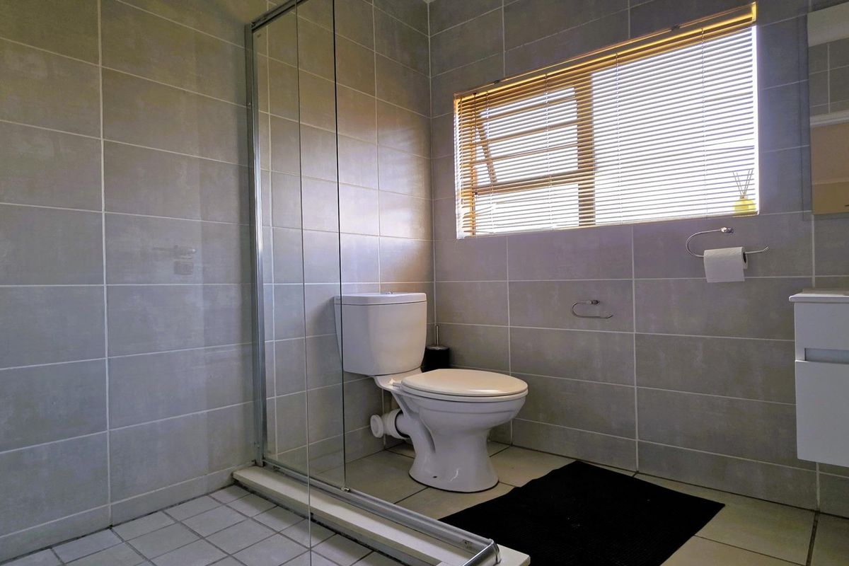 A modern bathroom featuring a glass-enclosed shower, a white vanity cabinet, and neutral wall tiling with a window for natural light.