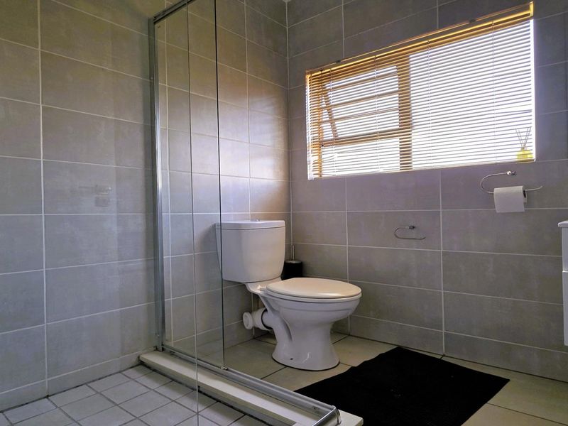 A modern bathroom featuring a glass-enclosed shower, a white vanity cabinet, and neutral wall tiling with a window for natural light.