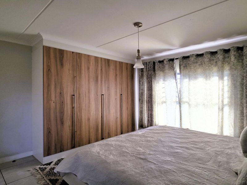 A well-maintained bedroom featuring modern wood-finish built-in cupboards, tiled flooring, and a pendant light fixture.