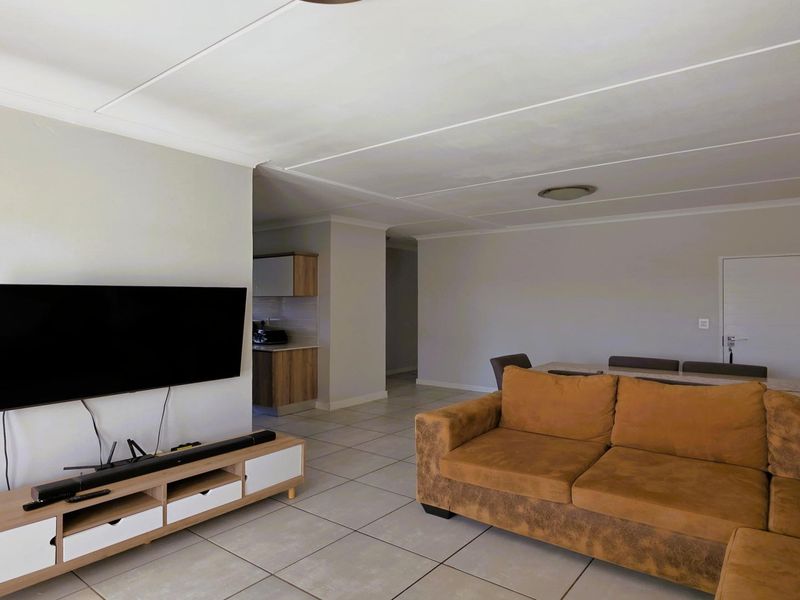 Open plan living and dining area featuring neutral tiled flooring and a coved ceiling, with a partial view into the kitchen area.
