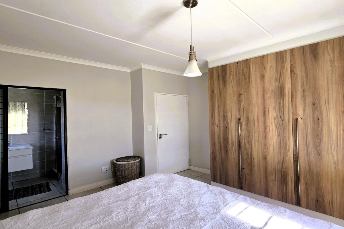 Spacious bedroom featuring modern wood-finish built-in cupboards, tiled flooring, and direct access to an en-suite bathroom.