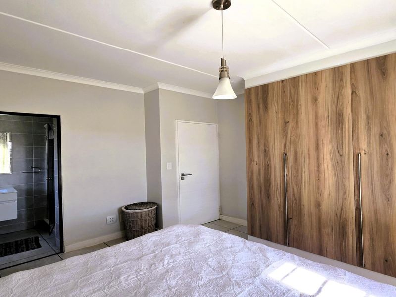 Spacious bedroom featuring modern wood-finish built-in cupboards, tiled flooring, and direct access to an en-suite bathroom.