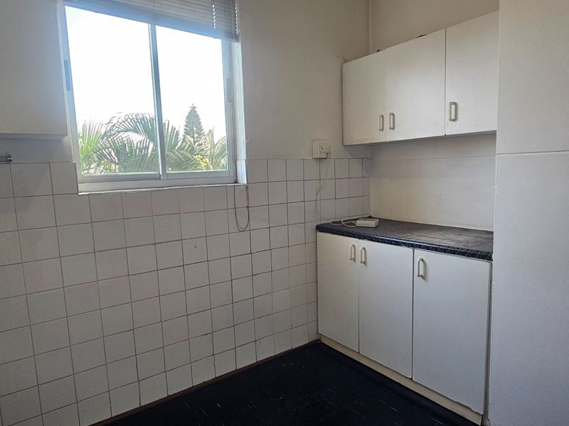 A compact, empty kitchen featuring white built-in cabinetry, dark laminate countertops, and a tiled backsplash, offering a blank canvas for renovation.