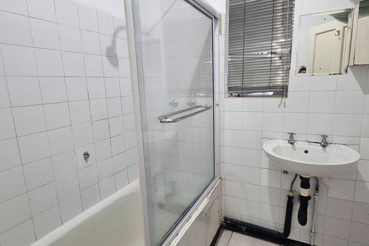 A dated bathroom featuring a bathtub with a glass screen, pedestal basin, and tiled walls, currently in need of renovation and cosmetic updates.
