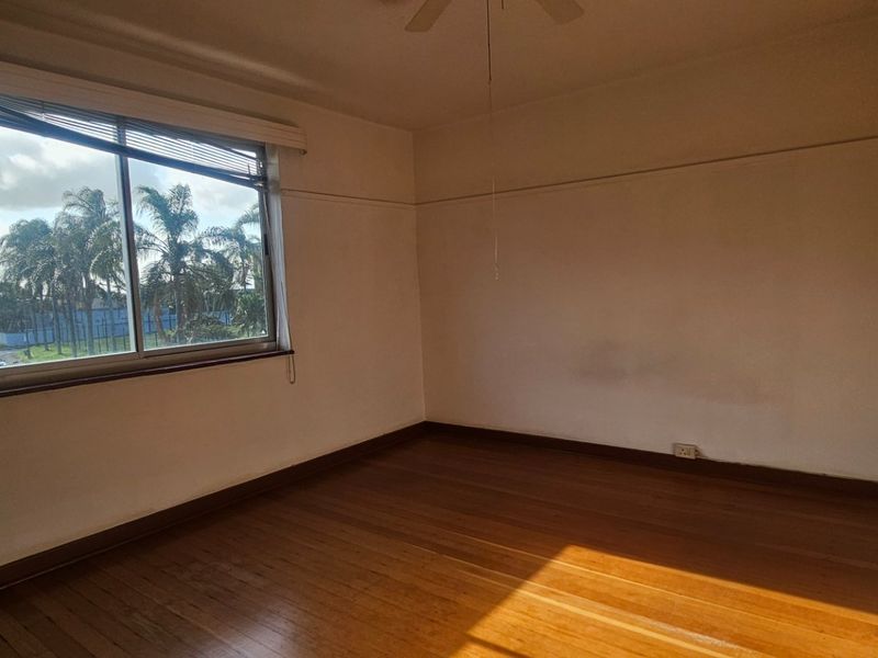 An empty bedroom featuring original hardwood flooring, built-in cupboards, a ceiling fan, and a large sliding window with exterior views.