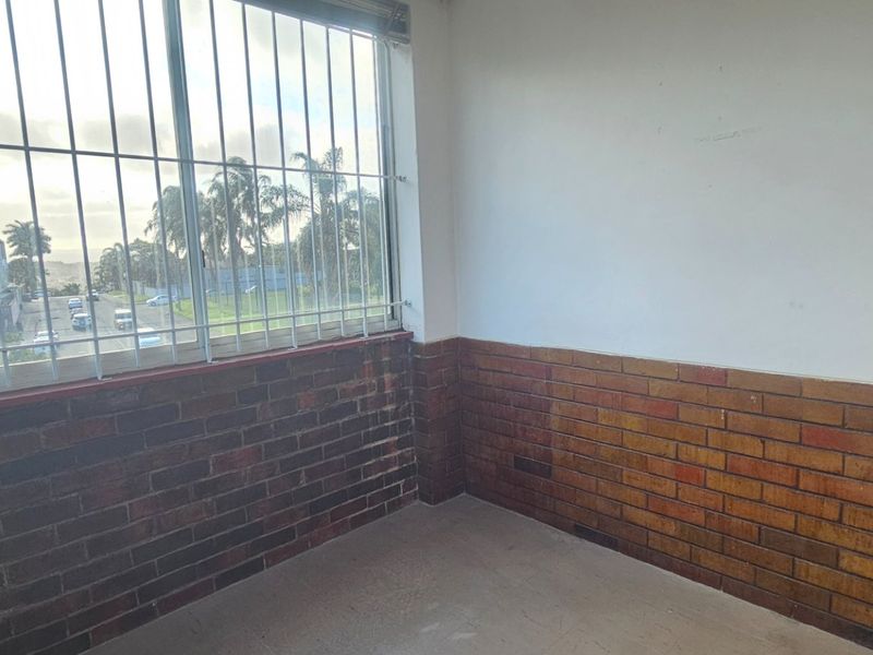 An empty bedroom featuring brick wall cladding, a large window with security bars, and neutral flooring, offering a blank canvas for renovation.