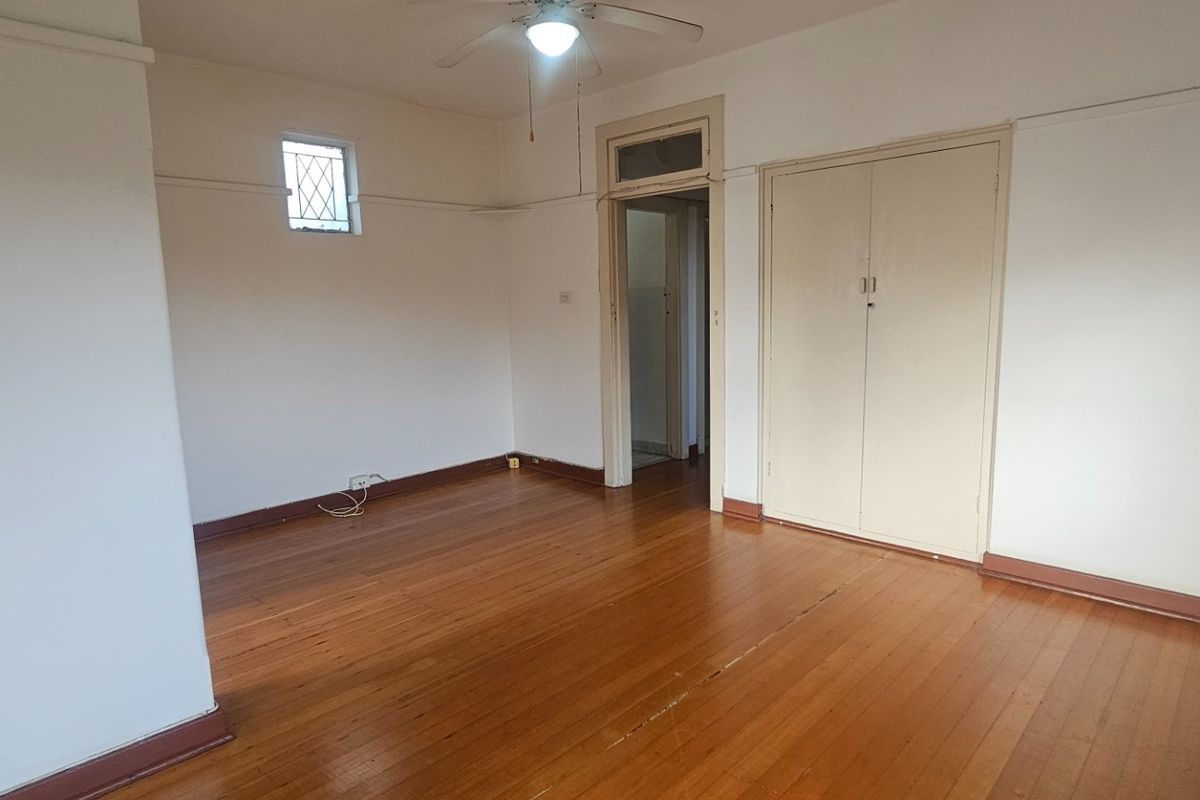 An empty bedroom featuring original timber flooring, a ceiling fan, and a built-in wardrobe, offering a blank canvas for renovation.