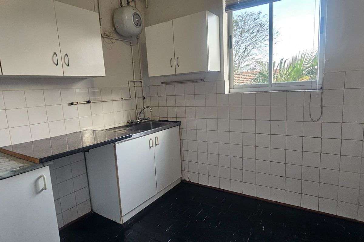 A functional, empty kitchen featuring white cabinetry, laminate countertops, tiled backsplash, and a wall-mounted water heater, ready for modernization.