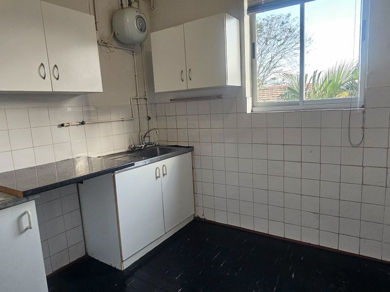 A functional, empty kitchen featuring white cabinetry, laminate countertops, tiled backsplash, and a wall-mounted water heater, ready for modernization.