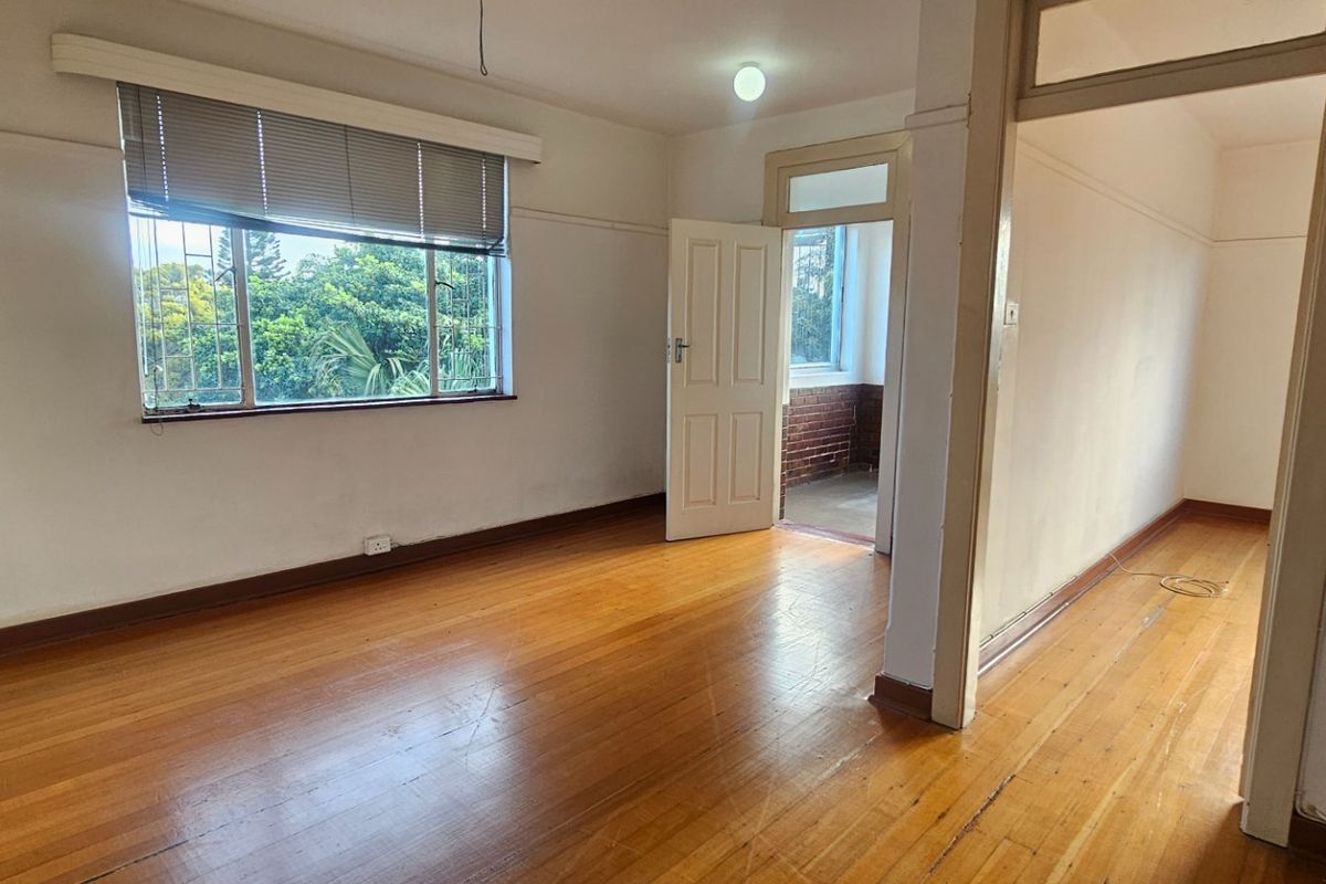 An empty living area featuring original hardwood flooring, neutral walls, and large windows with security bars, offering a bright and versatile blank canvas.