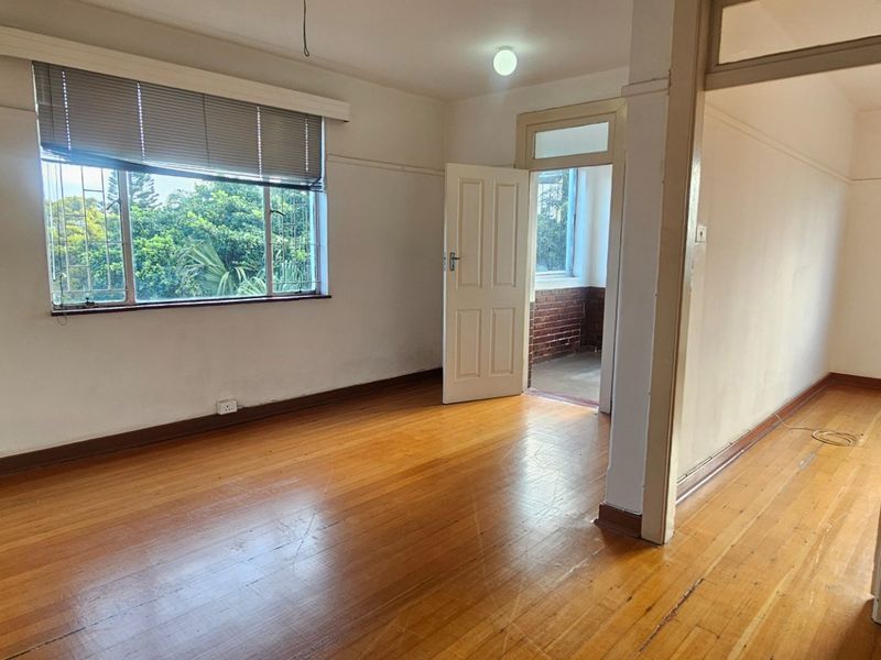 An empty living area featuring original hardwood flooring, neutral walls, and large windows with security bars, offering a bright and versatile blank canvas.