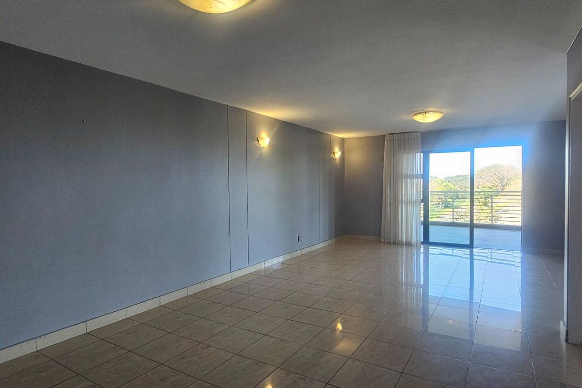 Spacious, empty living area featuring neutral tiled flooring, wall sconces, and a large sliding glass door providing access to an outdoor balcony.