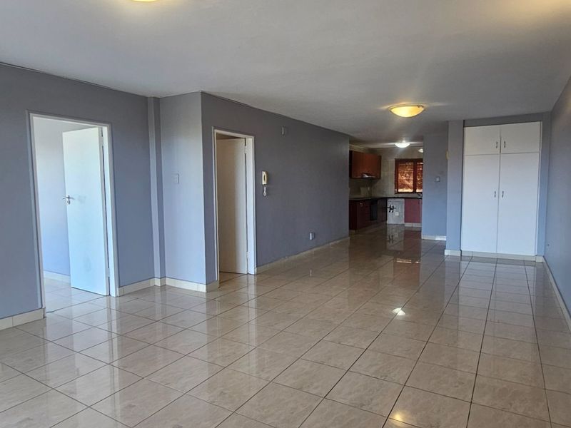 Spacious open-plan living area featuring neutral grey walls, tiled flooring, and built-in storage cupboards, leading through to a kitchen space.