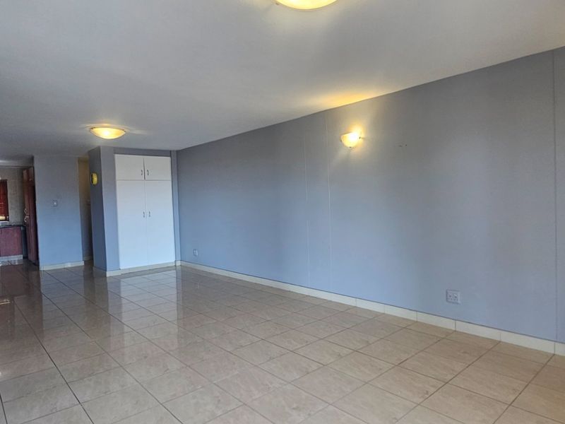 Spacious open-plan living area featuring neutral tiled flooring, built-in storage cupboards, and integrated wall and ceiling lighting.