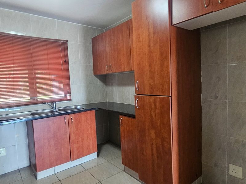 A functional kitchen featuring wooden cabinetry, granite countertops, a double sink, and tiled finishes throughout.