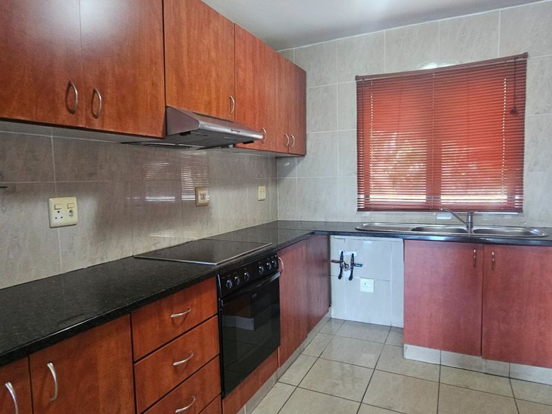 A functional kitchen featuring wood-finish cabinetry, granite countertops, a built-in oven with hob, and tiled finishes throughout.