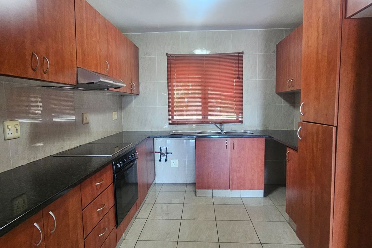 A functional kitchen featuring wood-finish cabinetry, dark granite countertops, built-in oven, extractor fan, and tiled finishes throughout.