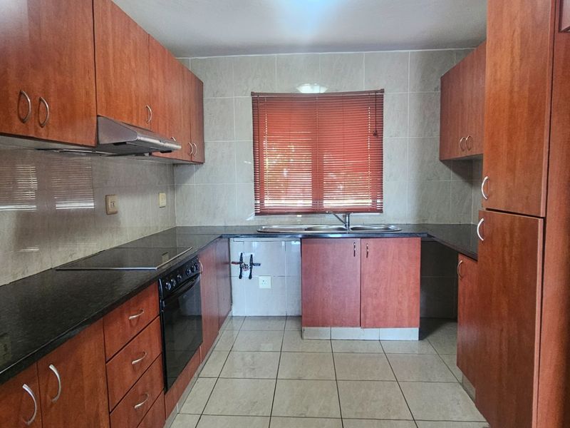 A functional kitchen featuring wood-finish cabinetry, dark granite countertops, built-in oven, extractor fan, and tiled finishes throughout.