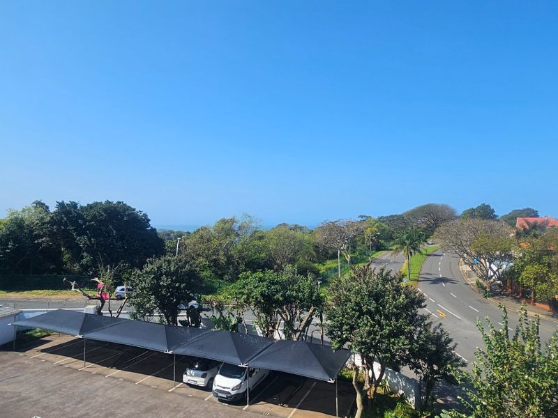 Elevated view overlooking a residential street, parking area with shade cloth carports, and surrounding greenery.