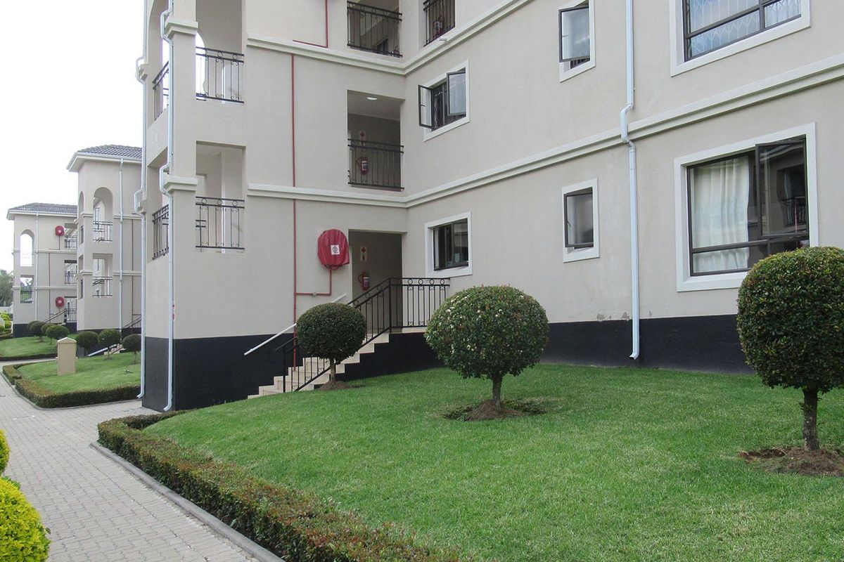 Exterior view of an apartment complex featuring a paved walkway, manicured lawn, and multi-story building facade with external fire safety equipment.