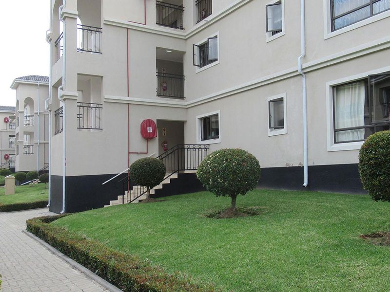 Exterior view of an apartment complex featuring a paved walkway, manicured lawn, and multi-story building facade with external fire safety equipment.