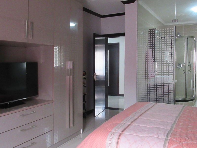 A modern bedroom featuring high-gloss built-in wardrobes and an integrated en-suite bathroom with a glass-enclosed shower and contemporary tiling.