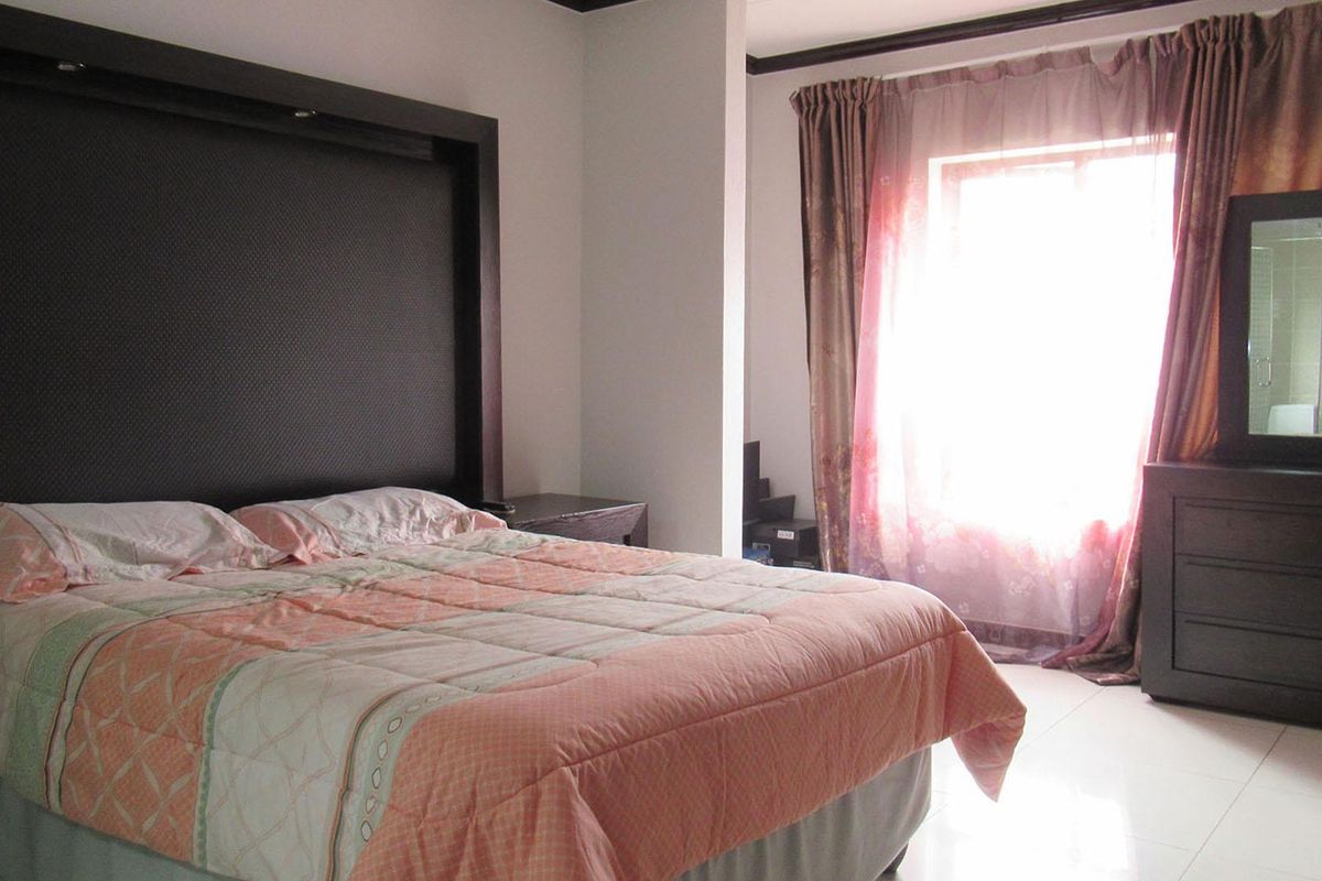 A bedroom featuring tiled flooring and a large built-in headboard, with natural light entering through a window.