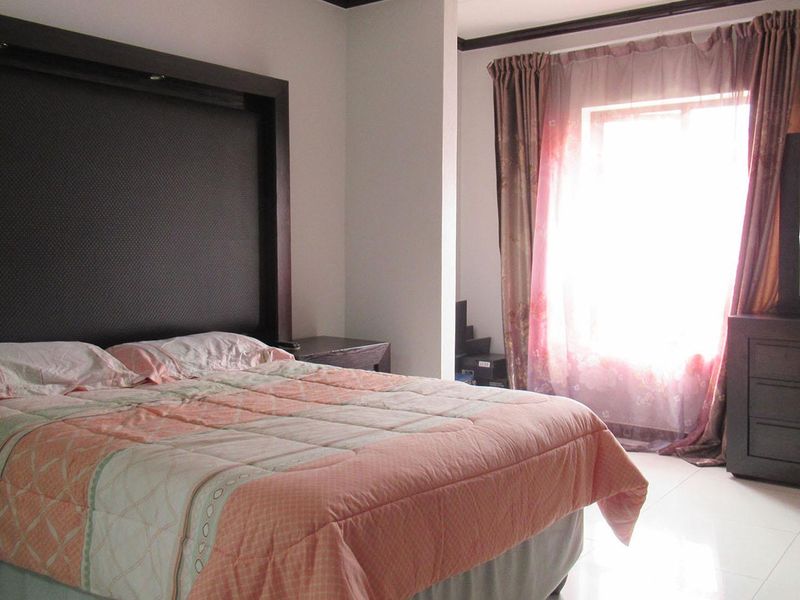 A bedroom featuring tiled flooring and a large built-in headboard, with natural light entering through a window.