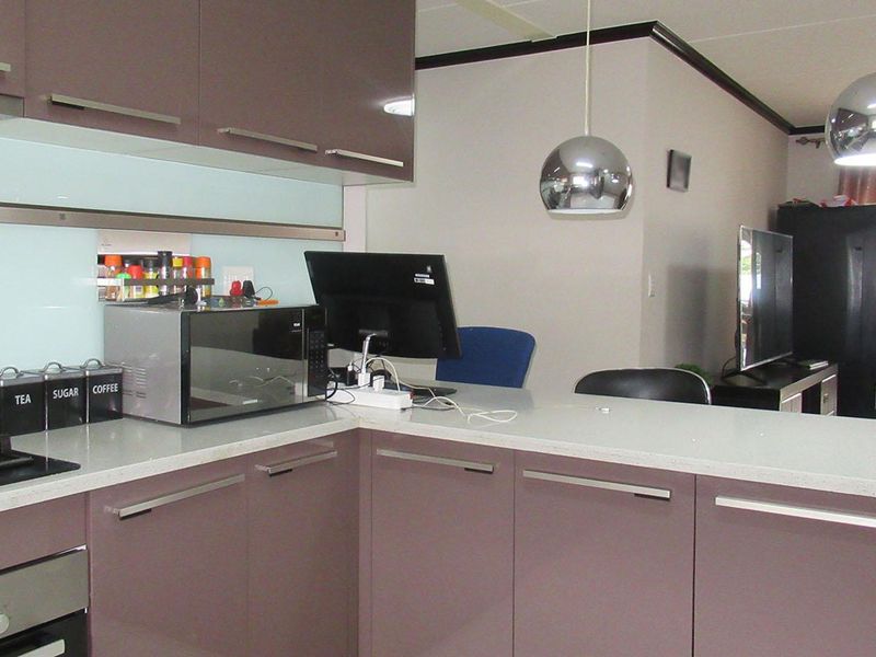 Open plan kitchen featuring modern purple cabinetry, stone countertops, integrated gas hob, and built-in oven, flowing into the adjacent living area.
