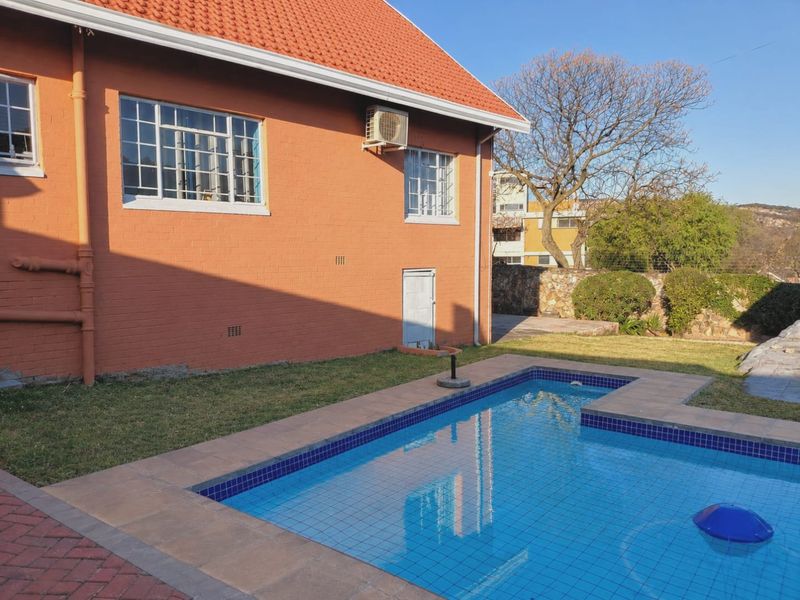 Rear exterior view featuring a swimming pool with tiled surround, set against a brick house with a tiled roof and external air conditioning unit.