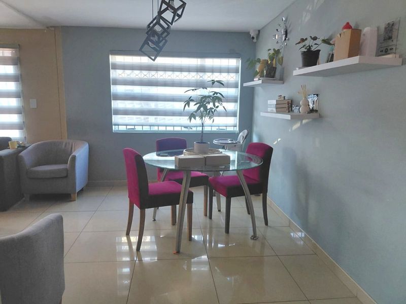 A bright dining area featuring large format floor tiles, modern roller blinds, and floating wall shelves, creating a functional and contemporary living space.