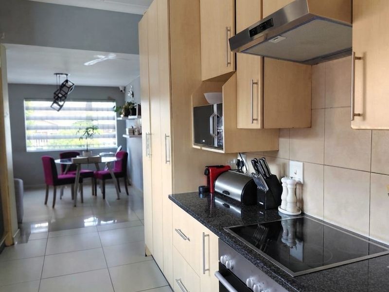 Open-plan kitchen featuring light wood cabinetry, granite countertops, and integrated appliances, flowing into a bright dining area with tiled flooring throughout.