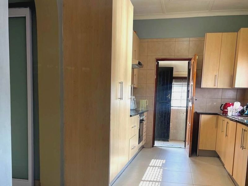 A functional kitchen featuring light wood-toned cabinetry, dark countertops, tiled backsplash, and tiled flooring, with an adjacent doorway leading to an exterior area.