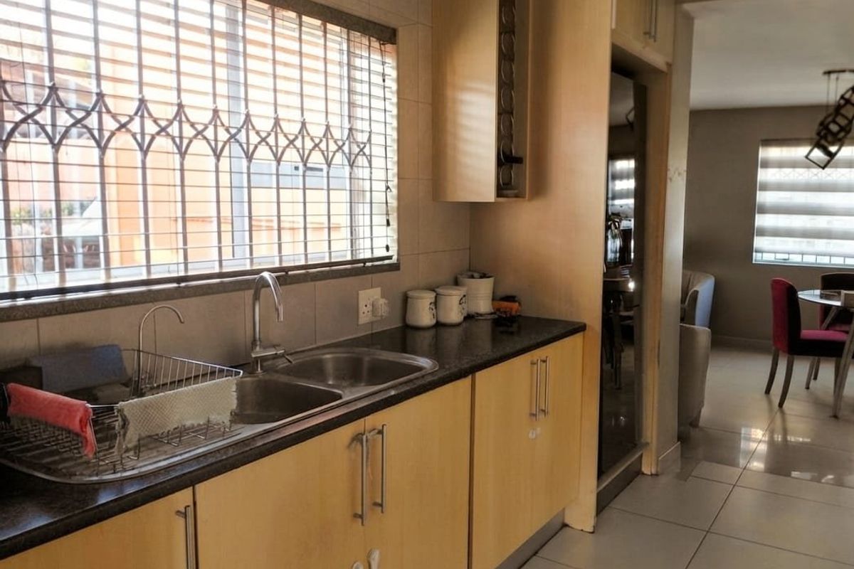 A functional kitchen featuring laminate cabinetry, granite countertops, and a double bowl sink, with a view through to the adjacent dining area.