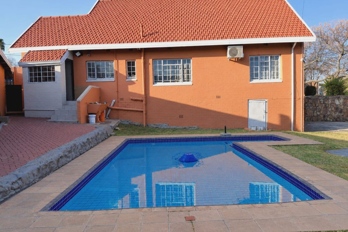 Rear view of the property featuring a swimming pool with tiled surround, brick facade, and terracotta roof tiles.