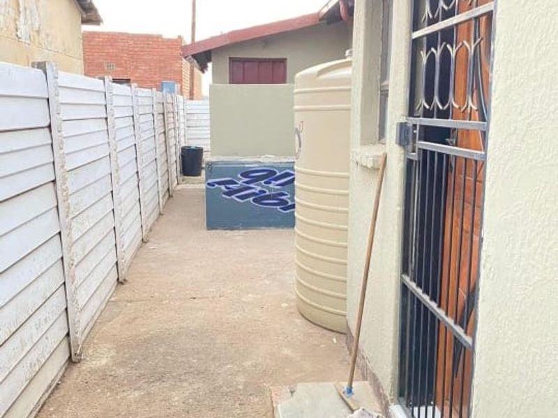 A narrow side passage featuring a precast concrete boundary wall, a water storage tank, and a security gate entrance.