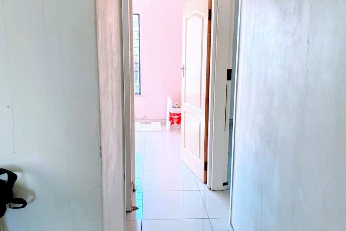 A narrow interior hallway featuring tiled flooring and ceiling ventilation, showing signs of wear on the wall surfaces.