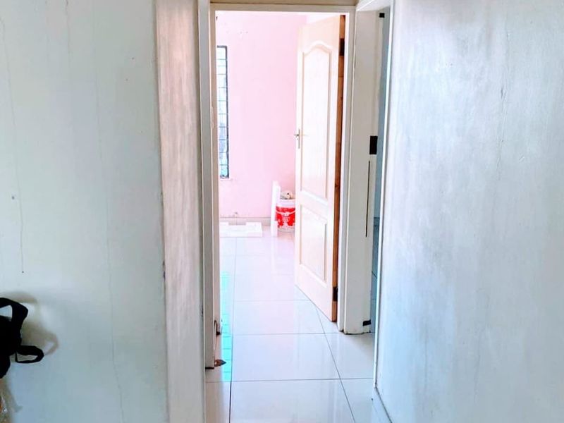 A narrow interior hallway featuring tiled flooring and ceiling ventilation, showing signs of wear on the wall surfaces.