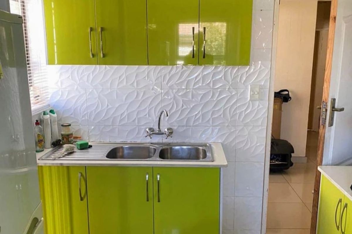 A compact kitchen featuring lime green high-gloss cabinetry, a double bowl sink, and textured white tiled splashbacks.