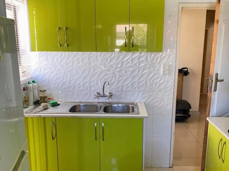 A compact kitchen featuring lime green high-gloss cabinetry, a double bowl sink, and textured white tiled splashbacks.