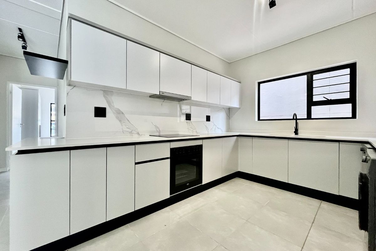 Modern, minimalist kitchen featuring white cabinetry, marble-look splashback, integrated appliances, and sleek black fixtures, offering a clean and contemporary aesthetic.