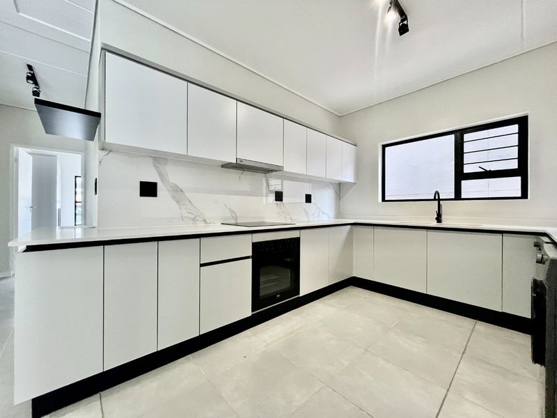 Modern, minimalist kitchen featuring white cabinetry, marble-look splashback, integrated appliances, and sleek black fixtures, offering a clean and contemporary aesthetic.