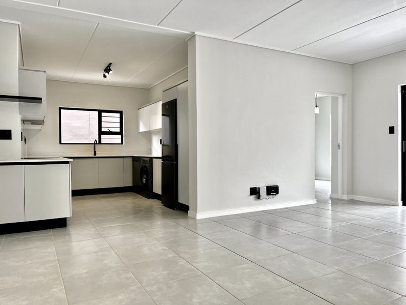 A bright, modern open-plan living and kitchen area featuring neutral tiled flooring, sleek cabinetry, and a clean, minimalist aesthetic throughout.